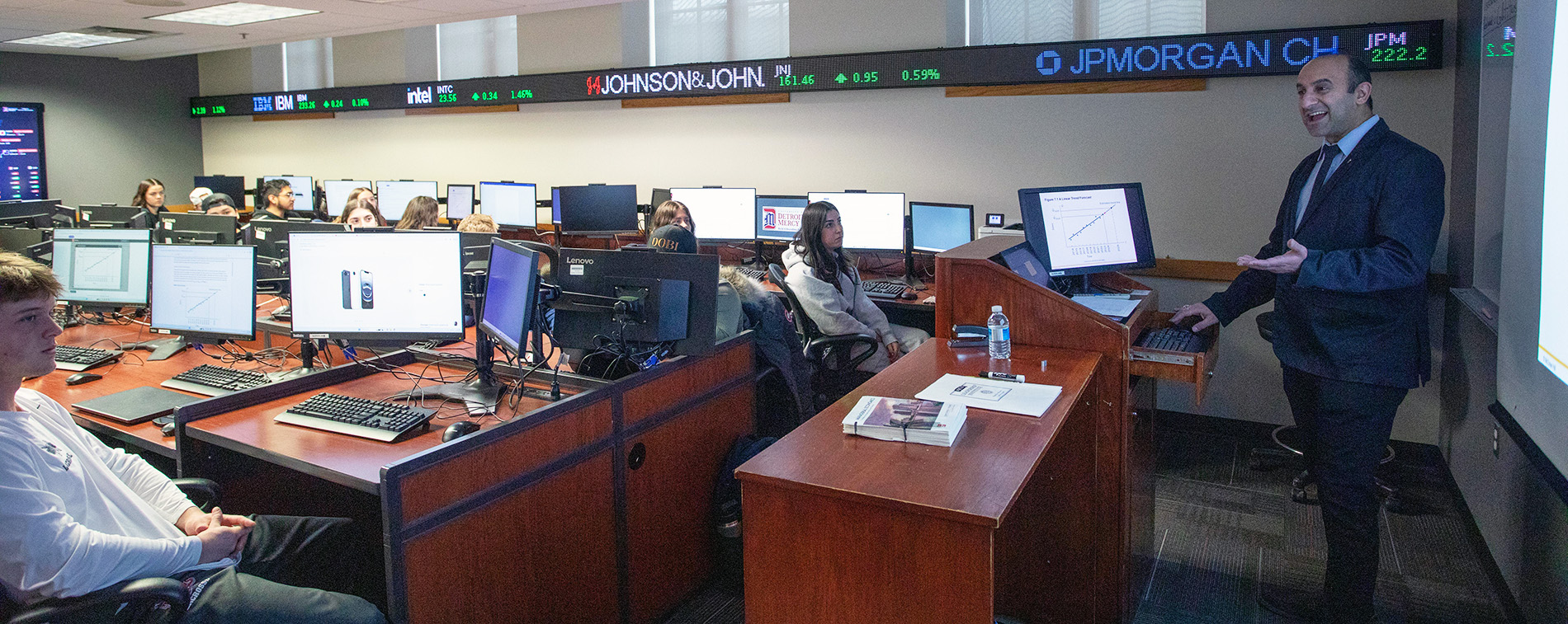 A professor teaches students in the Financial Market Lab